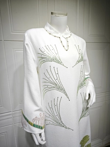 Detail of white textured dress featuring sparkling green rhinestone patterns and embroidery