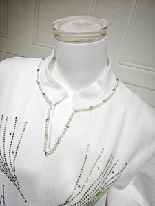 Close-up of V-neck white jacquard dress with pearl beads and green sequin embroidery