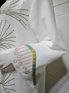 Detail of white crepe kaftan with green rhinestone fireworks and embroidered sleeve cuffs