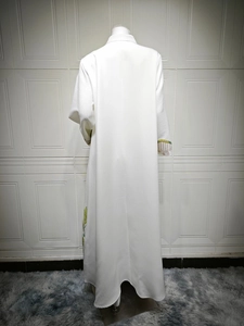 Detail of white long dress featuring colorful embroidery on cuffs and hemline side