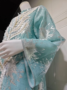 Detail von hellblauer Abaya mit silbernen Blumenmustern und weißen Blatt-Applikationen
