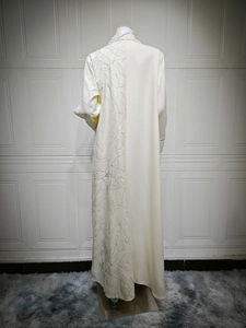 Detailed cream abaya with asymmetrical leaf patterns and smooth fabric texture close-up