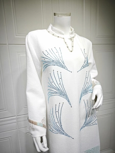 Detailed close-up of white jacquard dress with blue rhinestone feather pattern and embroidery