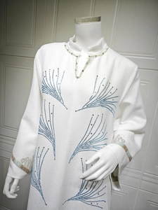 Detail of white jacquard dress with pearl collar decoration and blue rhinestone patterns