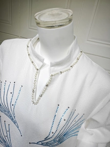 Detail of white jacquard dress with pearl collar and blue rhinestone patterns