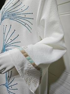 Detail of white dress featuring blue rhinestones and intricate ethnic embroidery on cuffs