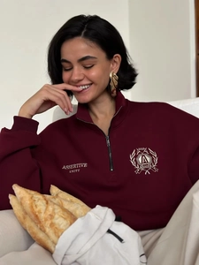 Detail of burgundy polo sweatshirt featuring metal zipper and white shield embroidery