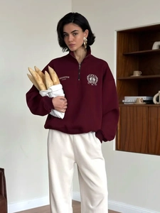 Detail of burgundy polo sweatshirt featuring embroidered shield emblem and zipper collar