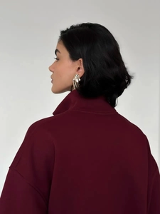 Detail of burgundy fleece sweatshirt featuring zip collar and gold artistic earrings