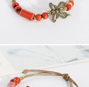 Macro detail of red ceramic beads and hollow bronze butterfly pendant on braided bracelet