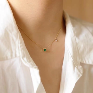 Dettaglio di una collana con ciondolo di smeraldo in oro indossata su camicia bianca