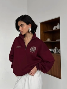 Detail of burgundy quarter-zip sweatshirt with varsity embroidery and ribbed cuffs