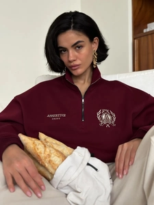 Detail of burgundy polo sweatshirt featuring embroidered college crest and white lettering