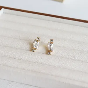 Makroansicht goldener geometrischer Ohrstecker mit Zirkonia auf beigem Samtstoff