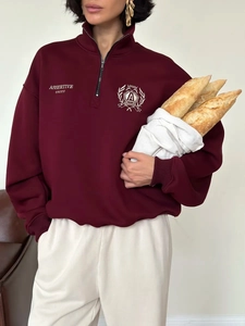 Detail of burgundy half-zip sweatshirt featuring white embroidery and collegiate crest