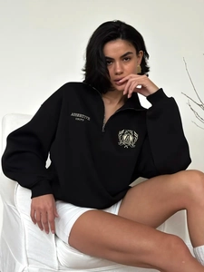 Detail of college style embroidery and half-zip design on black oversized sweatshirt