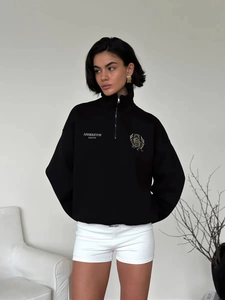 Detail of black half-zip sweatshirt featuring assertive unity embroidery and gold crest