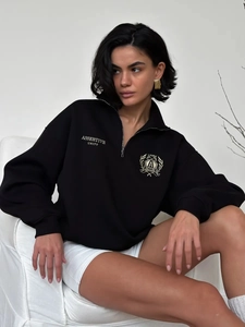 Detailed close-up of premium shield embroidery and half-zip collar on black oversized sweatshirt