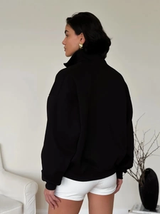 Side view of an oversized black polo sweatshirt with drop shoulders and ribbed cuffs