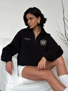 Close-up of black half-zip sweatshirt featuring white Assertive Unity graphic print