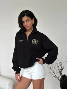Detail of black quarter-zip sweatshirt featuring college-style badge and logo print