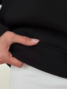 Close-up of the ribbed hem and soft fleece material on a black long sleeve polo sweatshirt