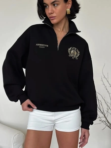 Detail shot of golden Assertive Unity embroidery on black half-zip fleece sweatshirt