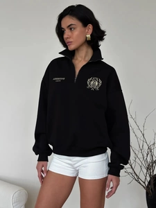 Detailed view of the college style embroidered shield badge and zipper on black polo sweatshirt