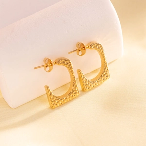 Detail of golden C-shaped stainless steel earrings with textured hammered finish on display