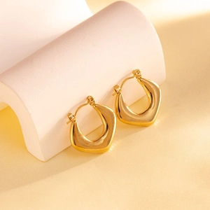 Detail of gold geometric U-shaped earrings with a polished mirror finish on a pedestal