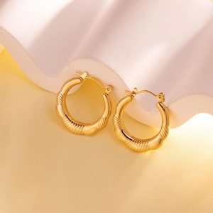 Close-up of golden ribbed hoop earrings with a polished finish on a white stone pedestal
