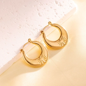 Close-up of gold crescent hoop earrings with sunburst engraving on silk background
