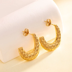 Detail of golden C-shaped earrings with unique hexagonal honeycomb texture and butterfly backs