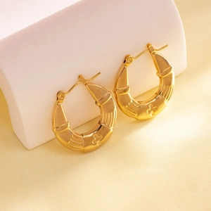 Detail of gold-plated geometric hoop earrings with vertical texture and cross relief