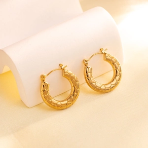 Close-up of golden geometric hoop earrings with textured honeycomb pattern on white stand