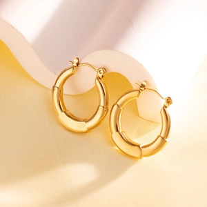 Detailed close-up of golden bamboo texture hoop earrings on a luxury silk background