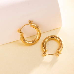 Close-up of golden geometric hoop earrings with textured diamond-cut pattern and clasp