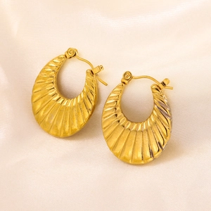Detailed close-up of golden geometric earrings with fan-shaped textures on satin fabric