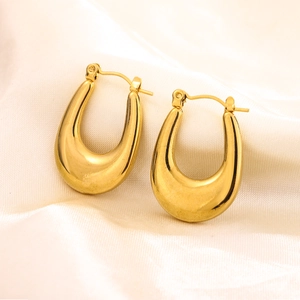 Macro shot of mirror-polished gold geometric U-shaped earrings on cream silk fabric