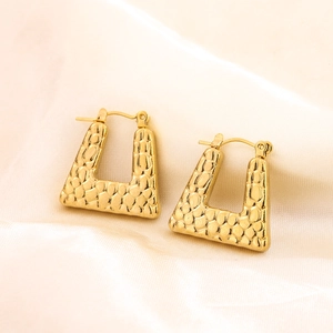 Macro detail of golden trapezoid earrings with textured crocodile pattern surface