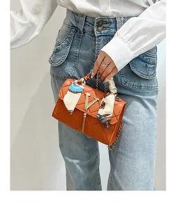 Detail of orange quilted crossbody bag featuring a silk scarf wrap handle and metal V-logo