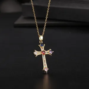 Macro view of a gold cross pendant featuring a red center stone and multicolor zircon gems