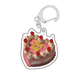 Detail of a pink heart cake acrylic keychain with white cream trim and a silver clasp