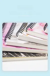 Close-up of thick A5 spiral notebooks with marble and pink gradient covers and twin-wire binding