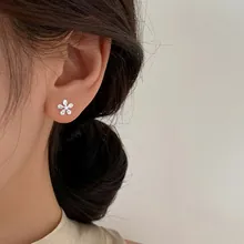 Dettaglio di un orecchino a fiore in argento con zirconi indossato sul lobo