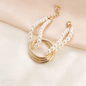 Detail of elegant double-layer pearl bracelet with intertwined gold rings on satin fabric