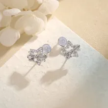 Macro shot of silver star stud earrings with blue beads and bow details on a beige surface