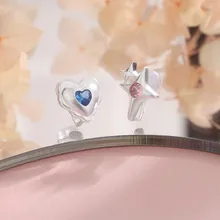 Asymmetric heart and star stud earrings with blue and pink gems on a reflective surface