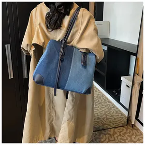 Close-up of contrast denim tote bag with leather straps worn by a model in trench coat