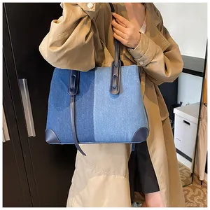 Detail of color-block denim tote bag featuring blue fabric patchwork and leather straps